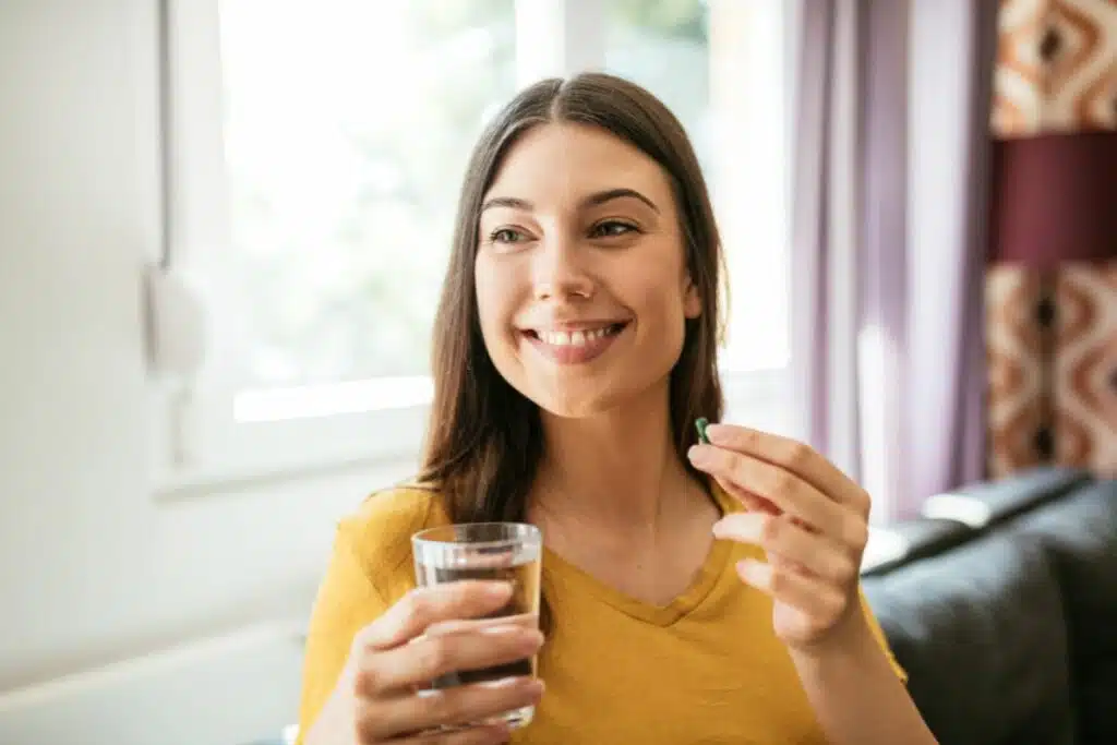 A woman taking a supplement capsule with a glass of water.
