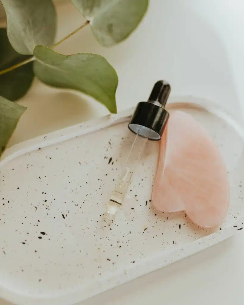 Close-up of a gua sha stone next to a dropper bottle of facial oil, illustrating skincare wellness and self-care rituals.